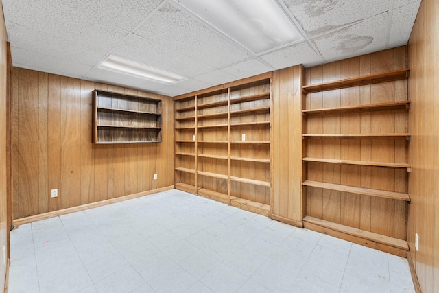 unfurnished room featuring built in shelves, a paneled ceiling, and wooden walls