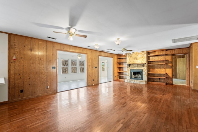 unfurnished living room featuring a stone fireplace, wooden walls, and built in shelves