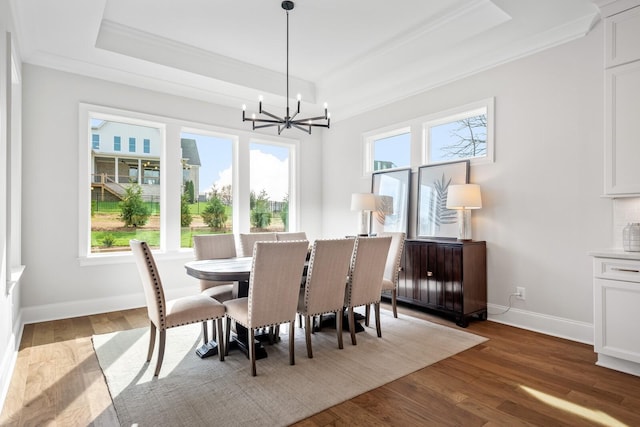 dining space featuring an inviting chandelier, ornamental molding, a tray ceiling, and hardwood / wood-style floors