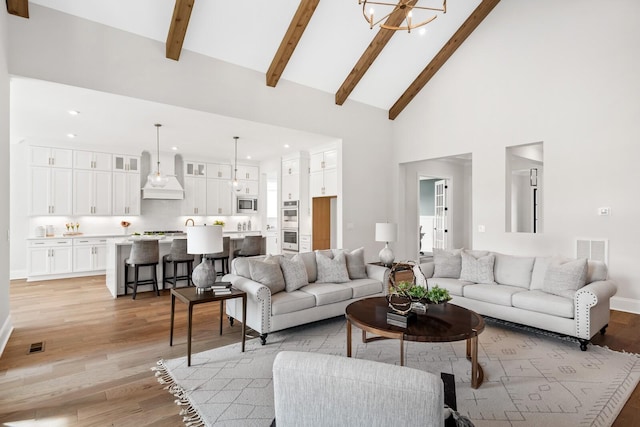 living room with a notable chandelier, beam ceiling, high vaulted ceiling, and light wood-type flooring