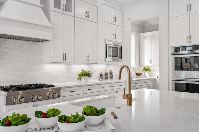 kitchen with tasteful backsplash, appliances with stainless steel finishes, white cabinets, and premium range hood