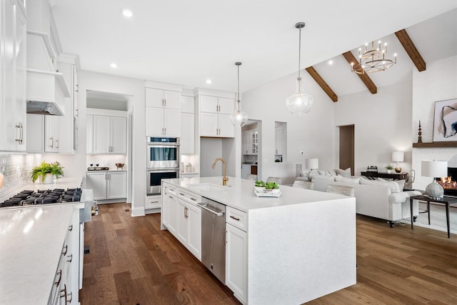 kitchen featuring appliances with stainless steel finishes, an island with sink, sink, white cabinets, and beam ceiling