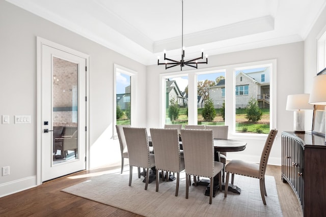 dining room with a raised ceiling, wood-type flooring, ornamental molding, and a chandelier