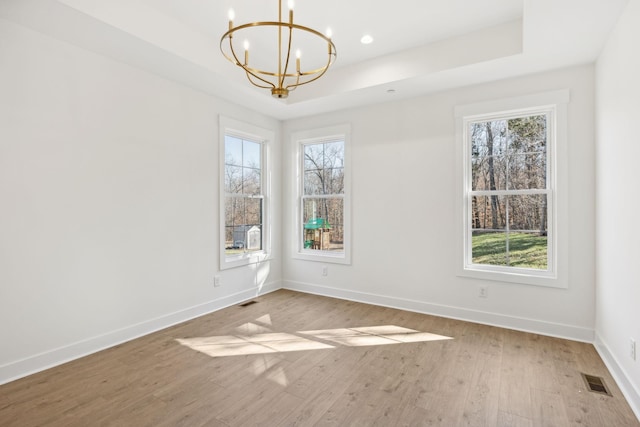 unfurnished room with light wood-type flooring, a healthy amount of sunlight, an inviting chandelier, and a tray ceiling