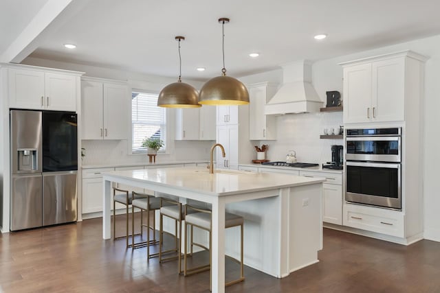 kitchen featuring appliances with stainless steel finishes, premium range hood, white cabinetry, sink, and pendant lighting