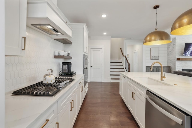 kitchen featuring appliances with stainless steel finishes, white cabinetry, decorative backsplash, hanging light fixtures, and custom range hood