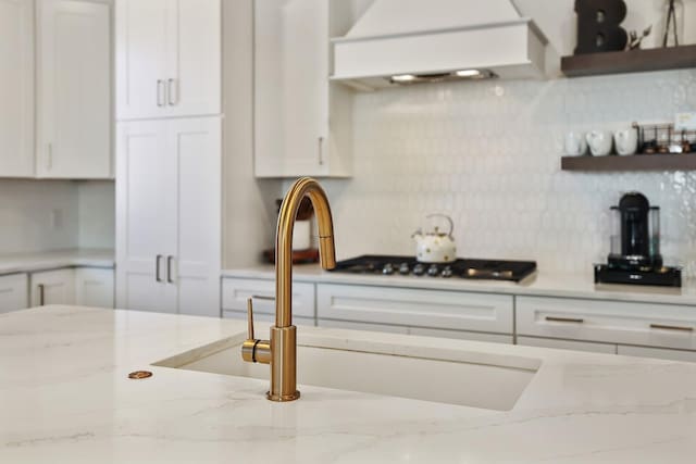 kitchen featuring premium range hood, white cabinetry, light stone countertops, and sink