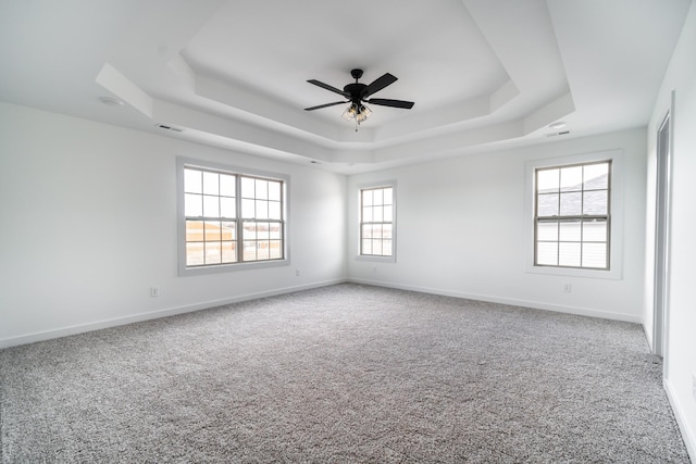 carpeted spare room featuring a ceiling fan, visible vents, a tray ceiling, and baseboards