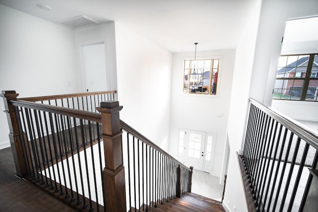 stairs featuring plenty of natural light, wood finished floors, visible vents, and an inviting chandelier