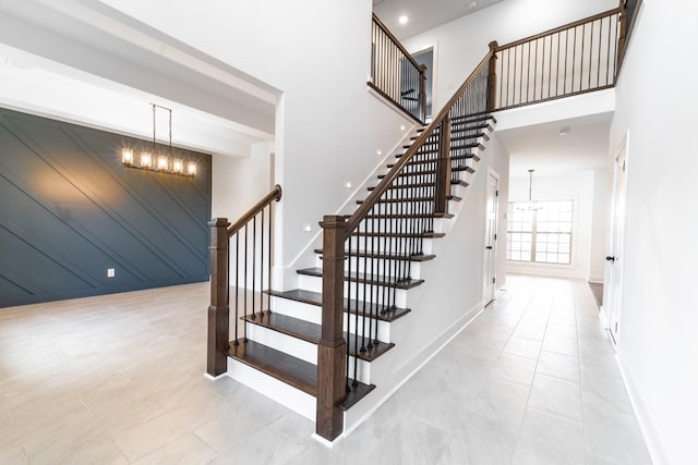 staircase with baseboards, a towering ceiling, and an inviting chandelier