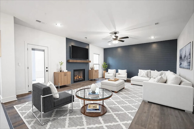 living area with visible vents, an accent wall, a large fireplace, wood finished floors, and baseboards