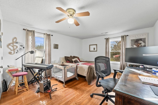 bedroom featuring ceiling fan, light hardwood / wood-style floors, a textured ceiling, and multiple windows