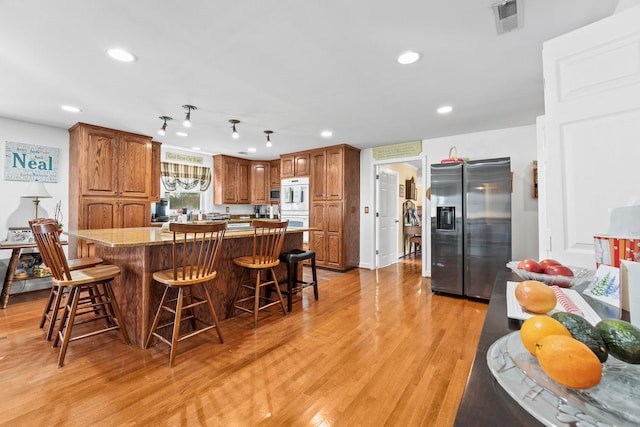 kitchen with a center island, a kitchen bar, light stone countertops, light hardwood / wood-style floors, and stainless steel refrigerator with ice dispenser