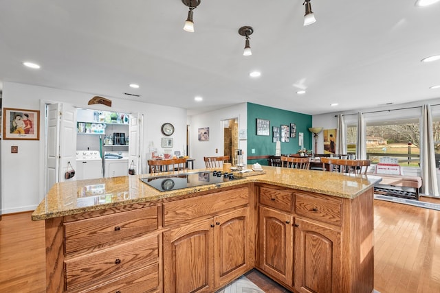 kitchen with black electric stovetop, a center island, washer and clothes dryer, and light stone countertops