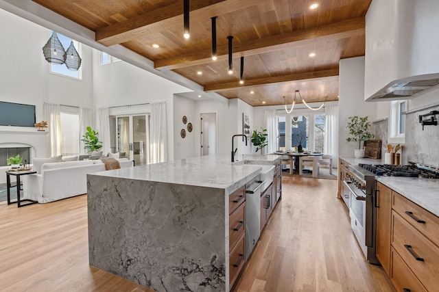 kitchen featuring high end stove, a large island with sink, wood ceiling, light stone countertops, and wall chimney range hood