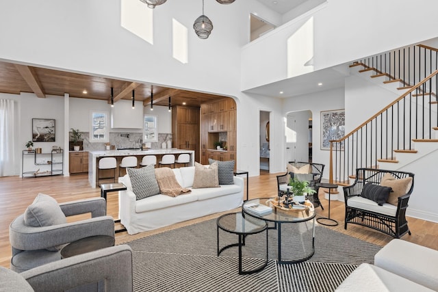 living room with beam ceiling, a high ceiling, wood ceiling, and light hardwood / wood-style flooring