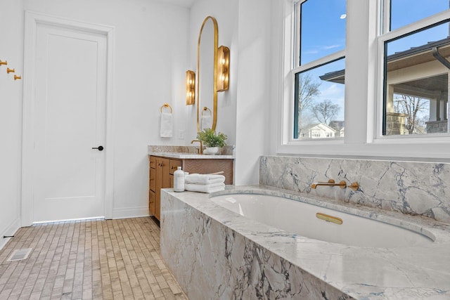 bathroom featuring a wealth of natural light, tiled bath, and vanity