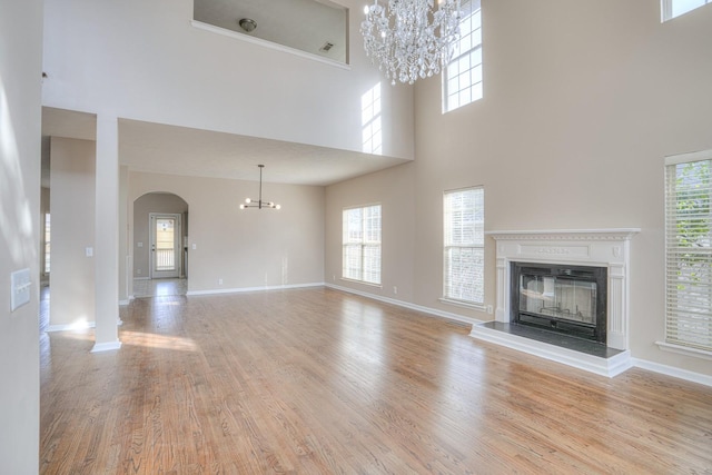 unfurnished living room with a towering ceiling, a notable chandelier, and light hardwood / wood-style floors