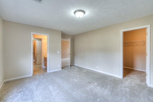 unfurnished bedroom with a walk in closet, light colored carpet, and a closet