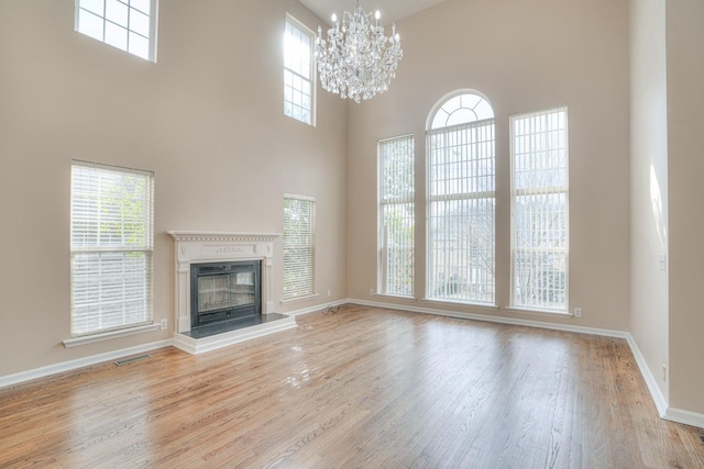 unfurnished living room featuring a high ceiling, a healthy amount of sunlight, an inviting chandelier, and light wood-type flooring