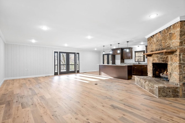 unfurnished living room with french doors, crown molding, a fireplace, and light hardwood / wood-style flooring