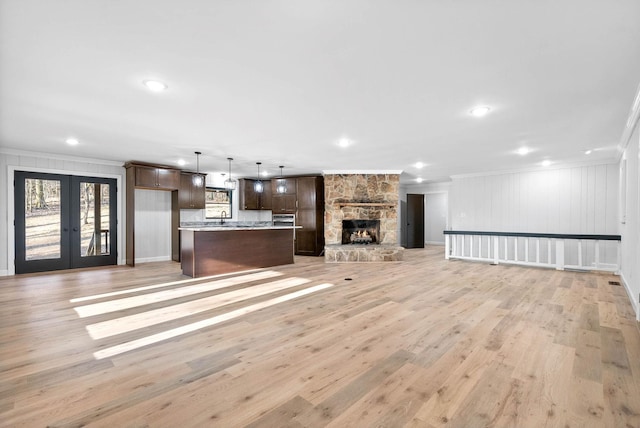 unfurnished living room featuring sink, ornamental molding, light hardwood / wood-style floors, a stone fireplace, and french doors