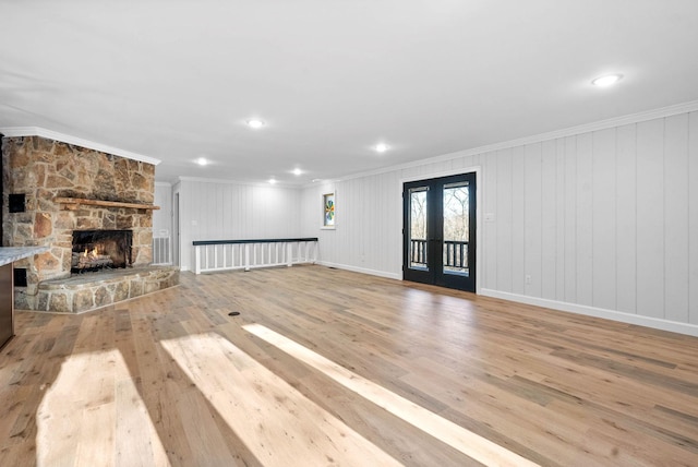 unfurnished living room with french doors, ornamental molding, a stone fireplace, and light wood-type flooring