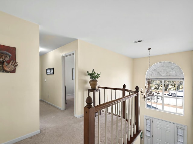 hallway with light carpet and a notable chandelier