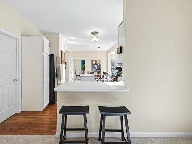 kitchen featuring a kitchen bar, black refrigerator with ice dispenser, hanging light fixtures, kitchen peninsula, and white cabinets