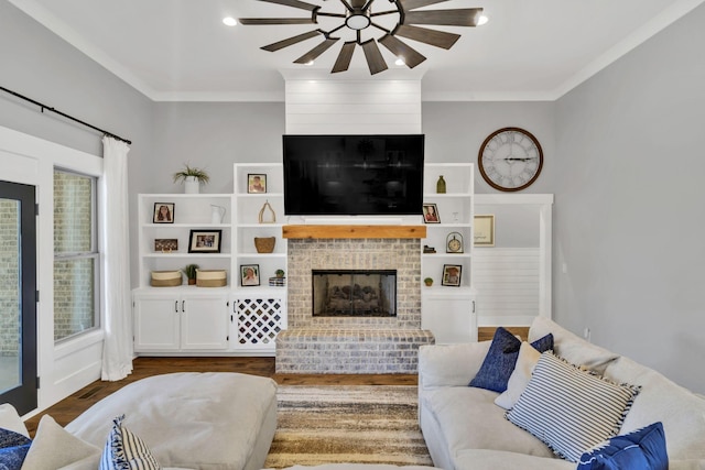 living room featuring a brick fireplace, hardwood / wood-style flooring, ornamental molding, and ceiling fan