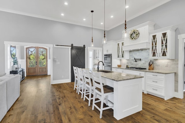 kitchen with a barn door, decorative light fixtures, a kitchen island with sink, and white cabinets