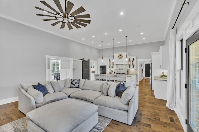 living room featuring crown molding, a barn door, dark wood-type flooring, and ceiling fan