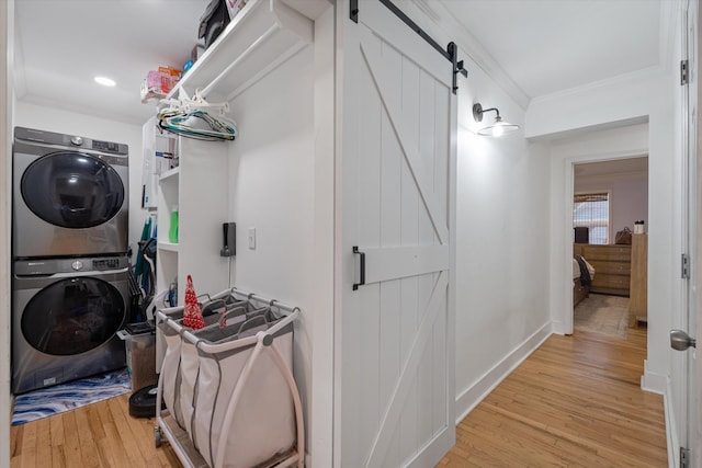 laundry area featuring crown molding, light wood-type flooring, stacked washer and clothes dryer, and a barn door