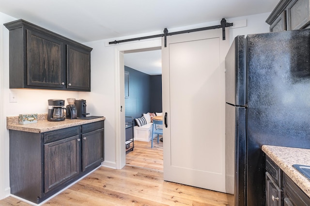 kitchen with black fridge, dark brown cabinetry, a barn door, and light wood-type flooring