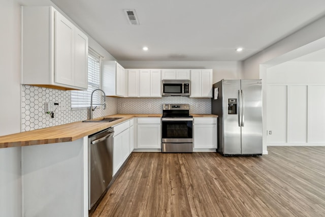 kitchen with butcher block counters, sink, white cabinets, light hardwood / wood-style floors, and stainless steel appliances