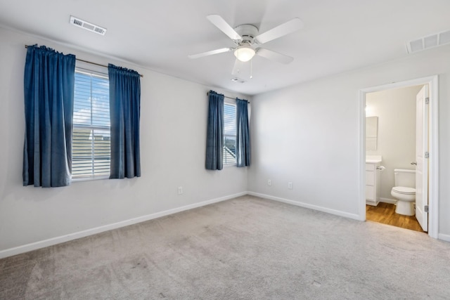 unfurnished bedroom featuring ceiling fan, ensuite bathroom, light colored carpet, and multiple windows