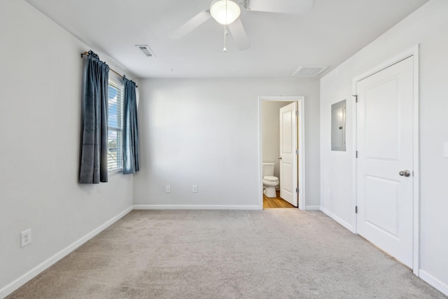 unfurnished bedroom featuring connected bathroom, light colored carpet, ceiling fan, and electric panel