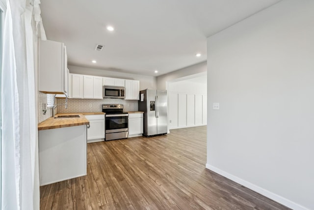 kitchen with butcher block countertops, white cabinets, backsplash, light hardwood / wood-style floors, and stainless steel appliances