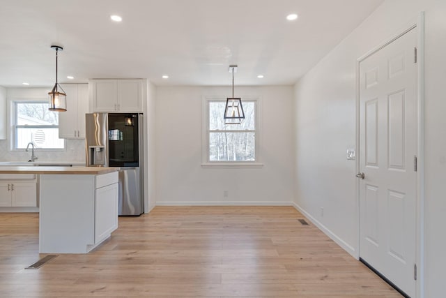 kitchen featuring stainless steel fridge with ice dispenser, light hardwood / wood-style flooring, pendant lighting, decorative backsplash, and white cabinets