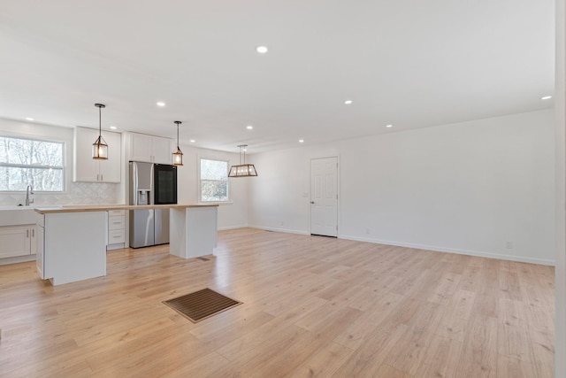 kitchen featuring hanging light fixtures, a center island, white cabinets, and stainless steel fridge