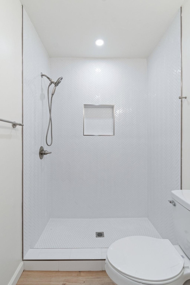 bathroom featuring hardwood / wood-style flooring, toilet, and a tile shower