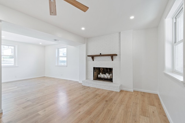 unfurnished living room with ceiling fan, a brick fireplace, and light wood-type flooring