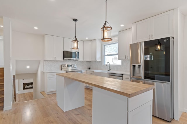 kitchen with a kitchen island, wood counters, tasteful backsplash, white cabinets, and stainless steel appliances