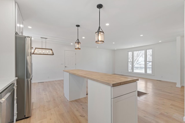 kitchen featuring stainless steel refrigerator, butcher block counters, hanging light fixtures, a center island, and white cabinets