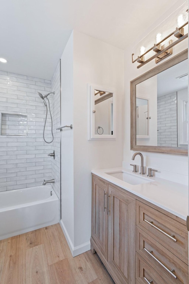 bathroom featuring wood-type flooring, tiled shower / bath combo, and vanity