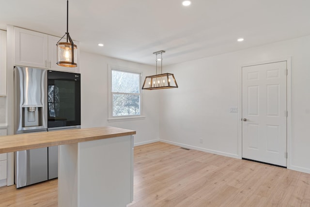 kitchen featuring white cabinetry, wood counters, stainless steel fridge, and decorative light fixtures