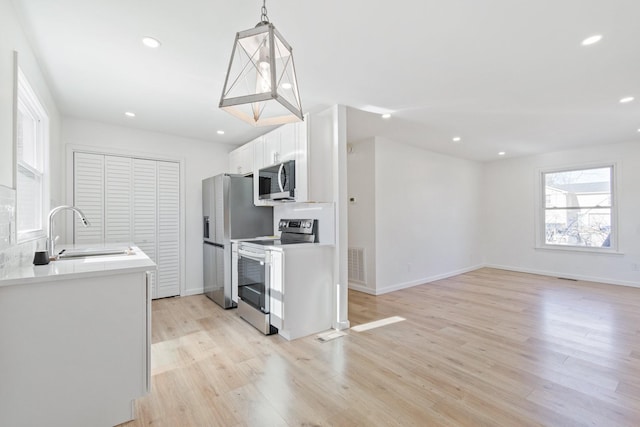 kitchen featuring sink, white cabinetry, hanging light fixtures, light hardwood / wood-style flooring, and stainless steel appliances