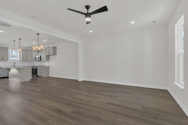 unfurnished living room with ceiling fan with notable chandelier and dark wood-type flooring