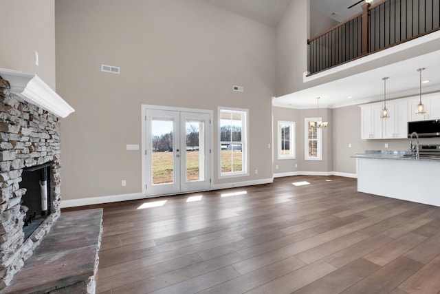 unfurnished living room featuring french doors, dark hardwood / wood-style flooring, a notable chandelier, a towering ceiling, and a fireplace