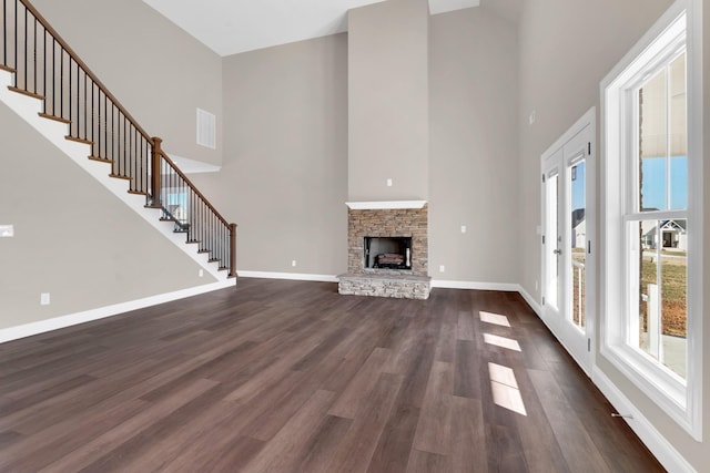 unfurnished living room featuring dark hardwood / wood-style flooring, a stone fireplace, and a high ceiling